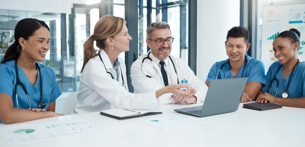 Médecins et infirmiers en réunion autour d'une table avec un ordinateur. Ils utilisent le logiciel Dragon Medical One.